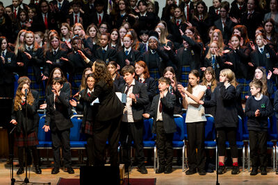 A woman directs a large group of young people singing
