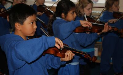 Four children in blue sweatshirts learn violins