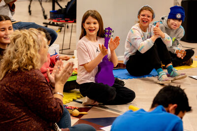 A group of children clap and hold colourful ukuleles